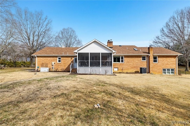 back of property with brick siding, a chimney, a lawn, central AC unit, and a sunroom