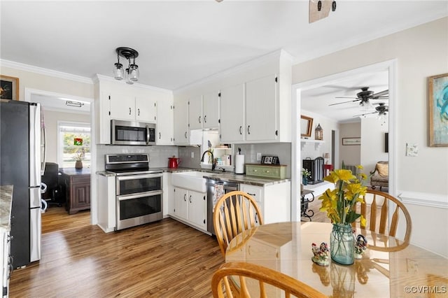 kitchen with crown molding, appliances with stainless steel finishes, white cabinetry, a sink, and wood finished floors