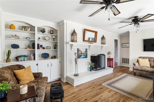 living room featuring a brick fireplace, built in features, visible vents, crown molding, and light wood-style floors