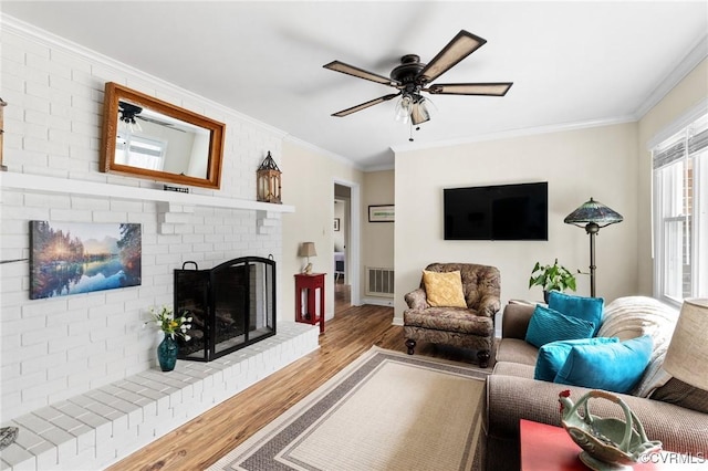 living room featuring crown molding, a fireplace, visible vents, and wood finished floors