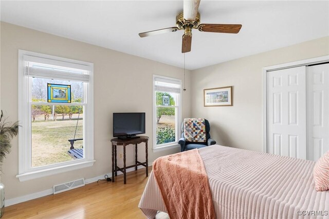 bedroom with light wood finished floors, a closet, visible vents, a ceiling fan, and baseboards