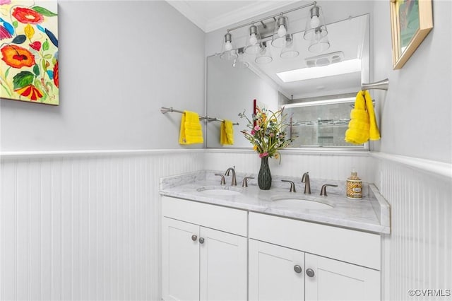 bathroom with double vanity, ornamental molding, a sink, and wainscoting