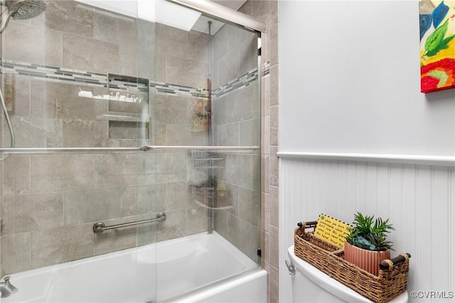 bathroom featuring wainscoting, toilet, and bath / shower combo with glass door