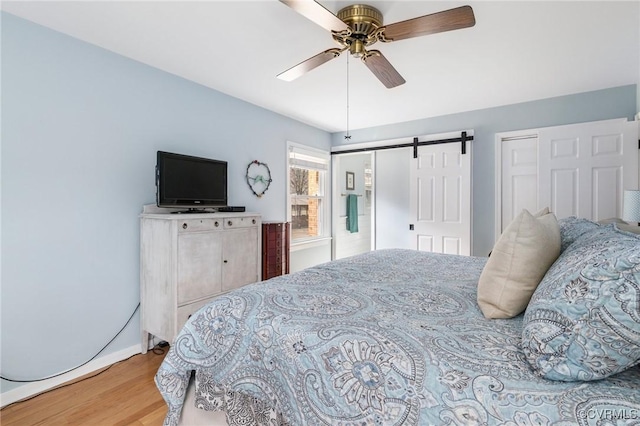 bedroom with a barn door, wood finished floors, a ceiling fan, and multiple closets