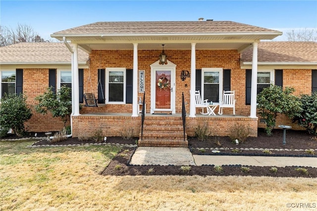 view of exterior entry featuring covered porch, a shingled roof, and brick siding