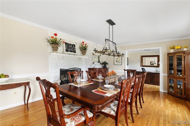 dining area with baseboards, a fireplace, crown molding, and light wood finished floors