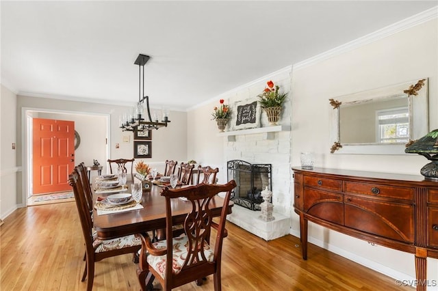 dining area featuring baseboards, crown molding, light wood-style floors, a fireplace, and a notable chandelier