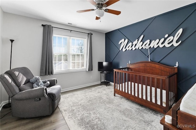 bedroom featuring ceiling fan, a crib, baseboards, and wood finished floors