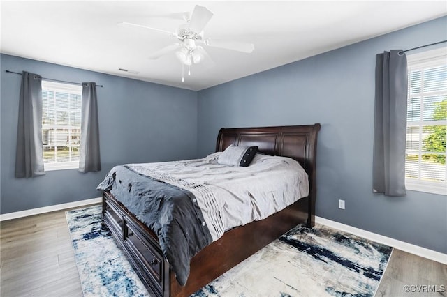 bedroom with a ceiling fan, multiple windows, baseboards, and wood finished floors