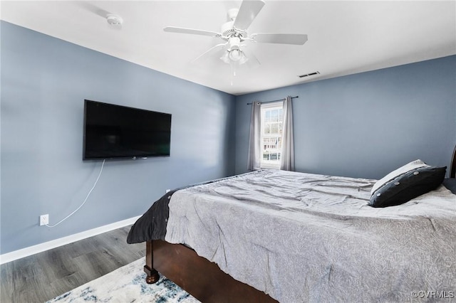 bedroom with a ceiling fan, visible vents, baseboards, and wood finished floors