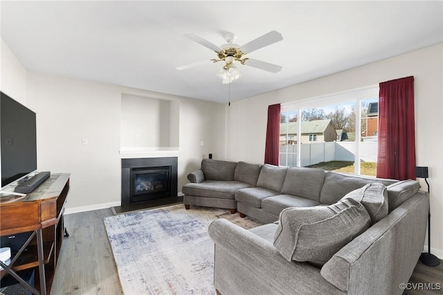 living room with ceiling fan, baseboards, wood finished floors, and a glass covered fireplace