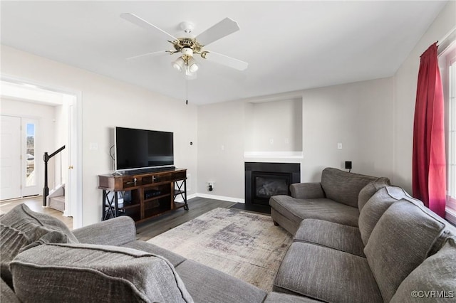 living area featuring stairway, a fireplace with flush hearth, ceiling fan, wood finished floors, and baseboards