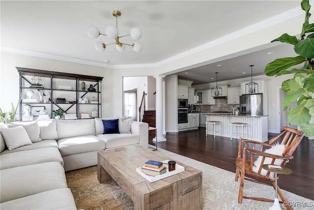 living area featuring a notable chandelier, dark wood-style flooring, stairway, decorative columns, and crown molding