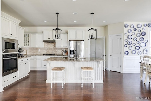 kitchen featuring light stone countertops, under cabinet range hood, appliances with stainless steel finishes, and a kitchen breakfast bar