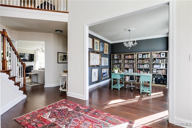 home office featuring baseboards, ornamental molding, wood finished floors, a fireplace, and a notable chandelier