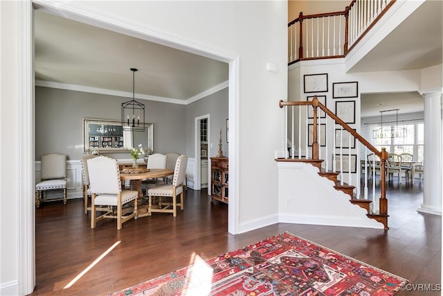 interior space featuring wood finished floors, baseboards, ornamental molding, an inviting chandelier, and ornate columns