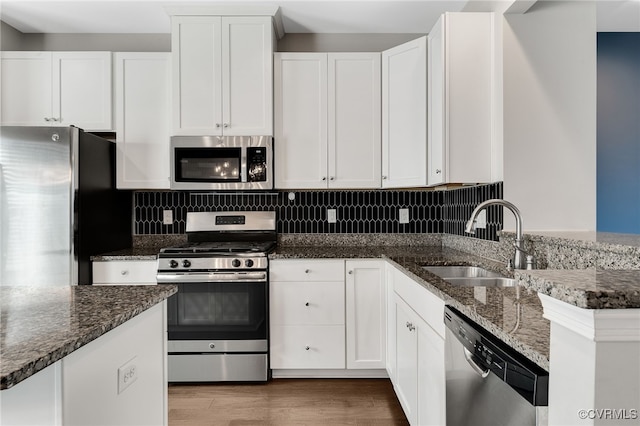 kitchen with stainless steel appliances, a sink, backsplash, and dark stone countertops