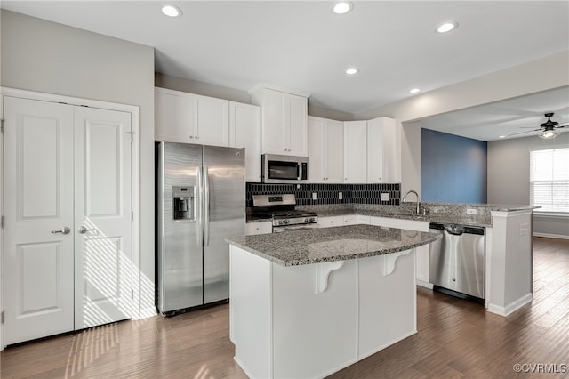 kitchen featuring stone counters, stainless steel appliances, decorative backsplash, a sink, and a peninsula