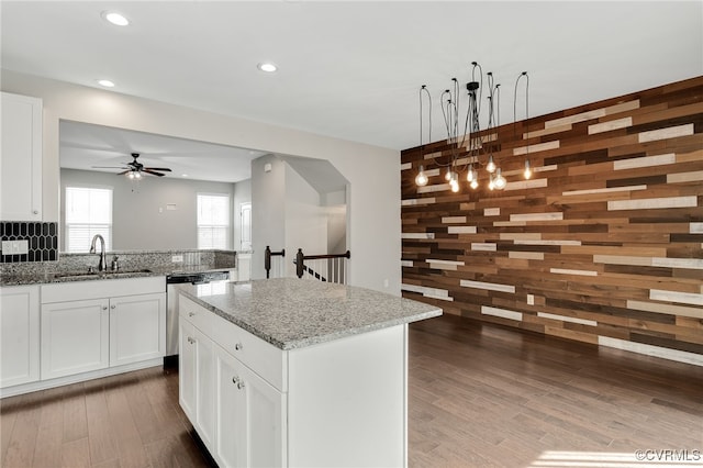 kitchen featuring wooden walls, dishwasher, a kitchen island, light stone counters, and a sink