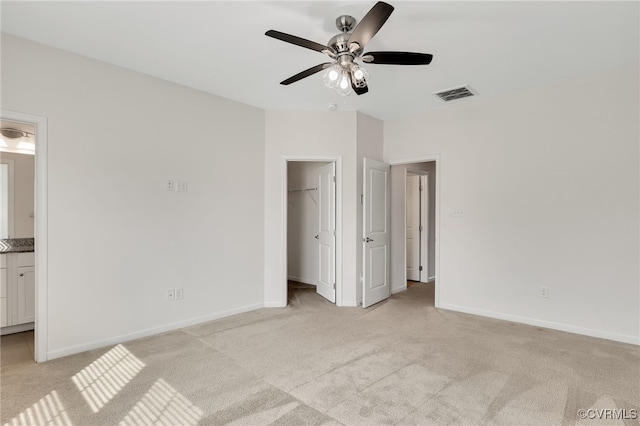 unfurnished bedroom with visible vents, a spacious closet, light carpet, connected bathroom, and baseboards