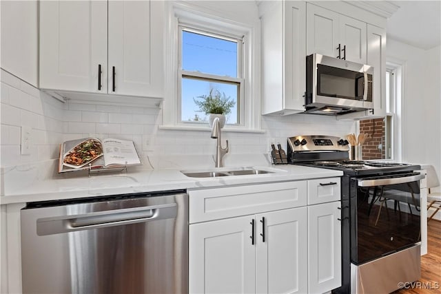 kitchen featuring light stone counters, decorative backsplash, appliances with stainless steel finishes, white cabinetry, and a sink