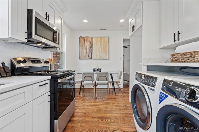 kitchen with stainless steel appliances, light countertops, light wood-style floors, white cabinets, and washer and dryer