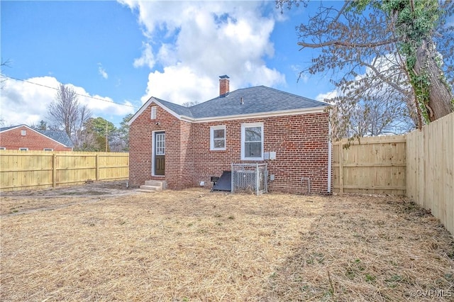 back of property with entry steps, brick siding, a chimney, and a fenced backyard