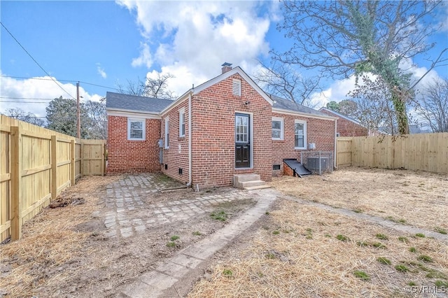 back of property with entry steps, a fenced backyard, a chimney, and brick siding