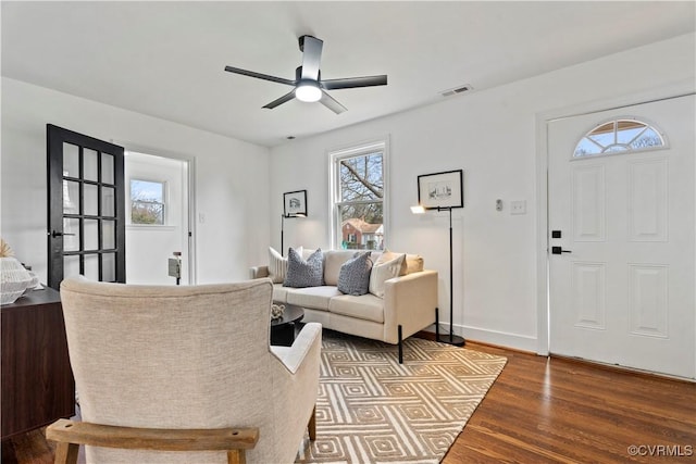 living area featuring baseboards, wood finished floors, visible vents, and a ceiling fan