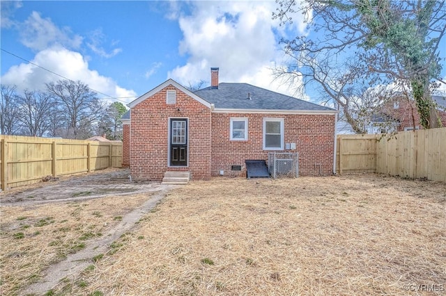 rear view of property featuring entry steps, brick siding, a chimney, and a fenced backyard