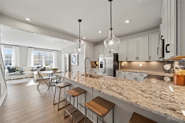 kitchen featuring stainless steel fridge with ice dispenser, light stone counters, a peninsula, a sink, and backsplash