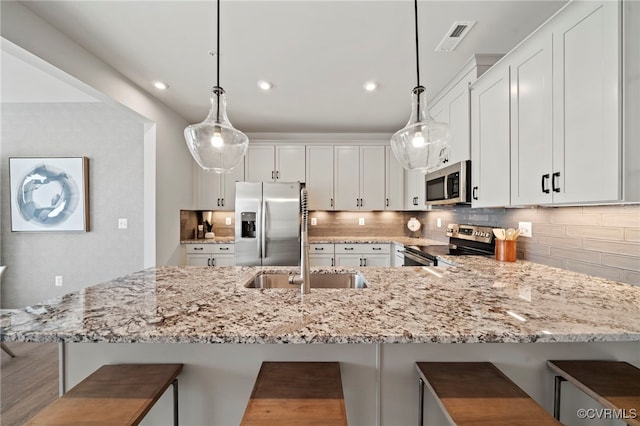 kitchen with stainless steel appliances, white cabinets, decorative backsplash, and light stone countertops