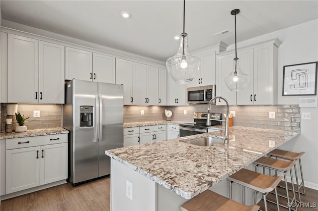 kitchen with a breakfast bar area, a peninsula, stainless steel appliances, light wood-style floors, and a sink