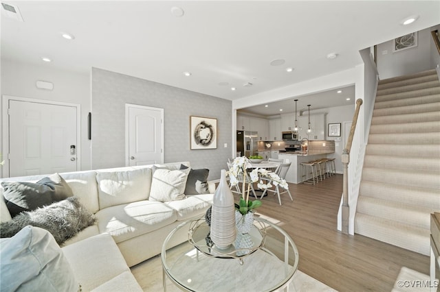 living room featuring light wood-style flooring, visible vents, stairway, and recessed lighting