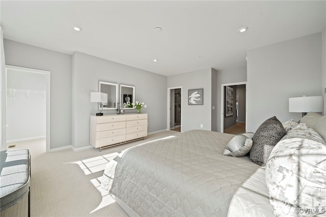 bedroom with a walk in closet, light carpet, baseboards, and recessed lighting