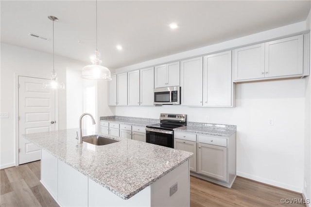 kitchen featuring stainless steel appliances, a sink, visible vents, light wood-style floors, and an island with sink