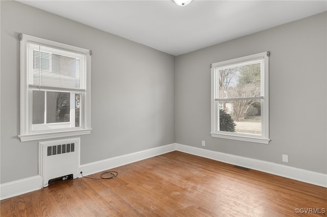 spare room featuring radiator heating unit, baseboards, and wood finished floors