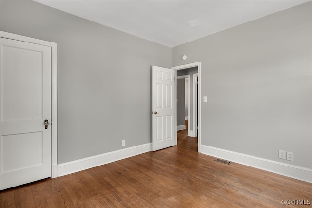 empty room featuring wood finished floors, visible vents, and baseboards