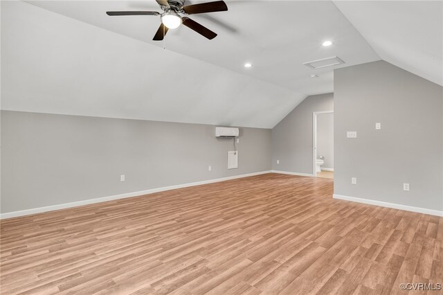 additional living space with baseboards, vaulted ceiling, an AC wall unit, light wood-style floors, and attic access