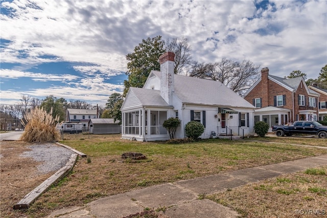 view of front facade featuring a chimney, a front yard, and a sunroom