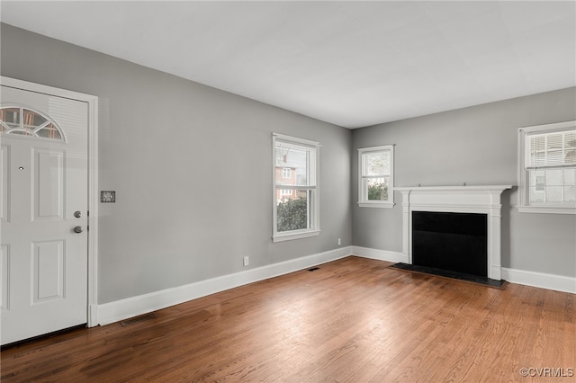 unfurnished living room featuring visible vents, a fireplace, baseboards, and wood finished floors