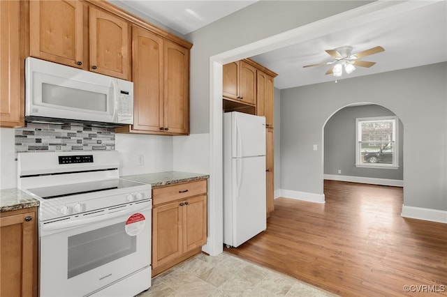 kitchen featuring white appliances, arched walkways, ceiling fan, light stone counters, and backsplash