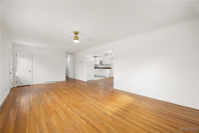 unfurnished living room featuring light wood-style flooring, a baseboard heating unit, a ceiling fan, baseboards, and crown molding