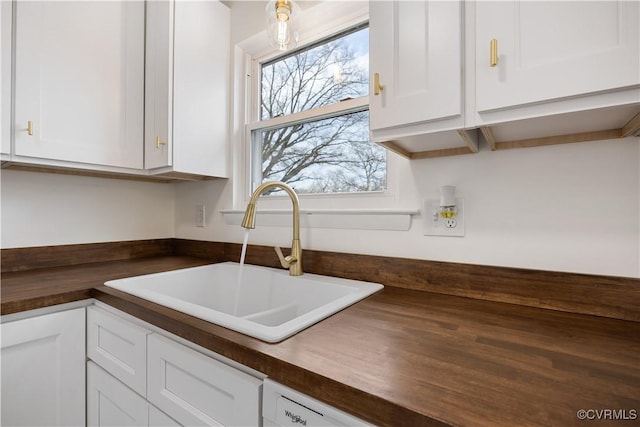 kitchen with butcher block countertops, white cabinetry, and a sink