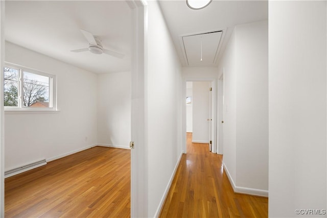 hallway featuring light wood finished floors, baseboard heating, attic access, and baseboards