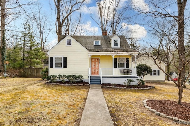 view of front facade with a chimney, a porch, roof with shingles, fence, and a front lawn