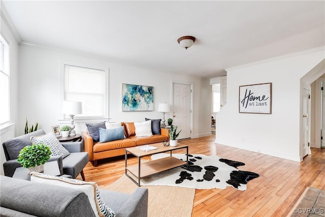 living area with light wood-style floors, a wealth of natural light, ornamental molding, and baseboards