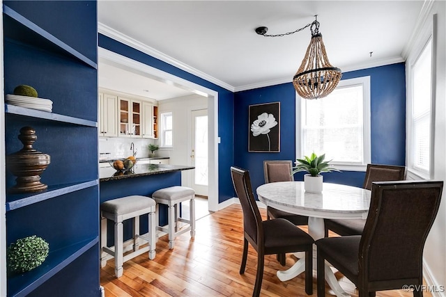 dining area with baseboards, light wood-type flooring, an inviting chandelier, and crown molding