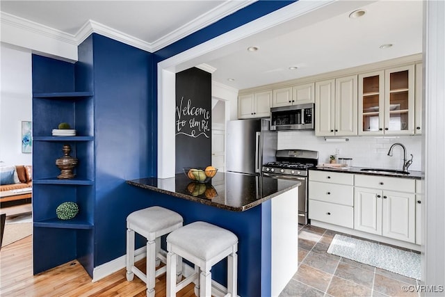 kitchen with ornamental molding, stainless steel appliances, a kitchen bar, open shelves, and a sink