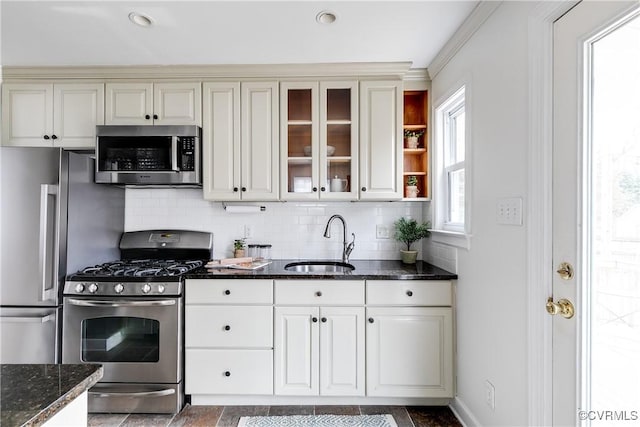 kitchen with stainless steel appliances, a sink, glass insert cabinets, and decorative backsplash